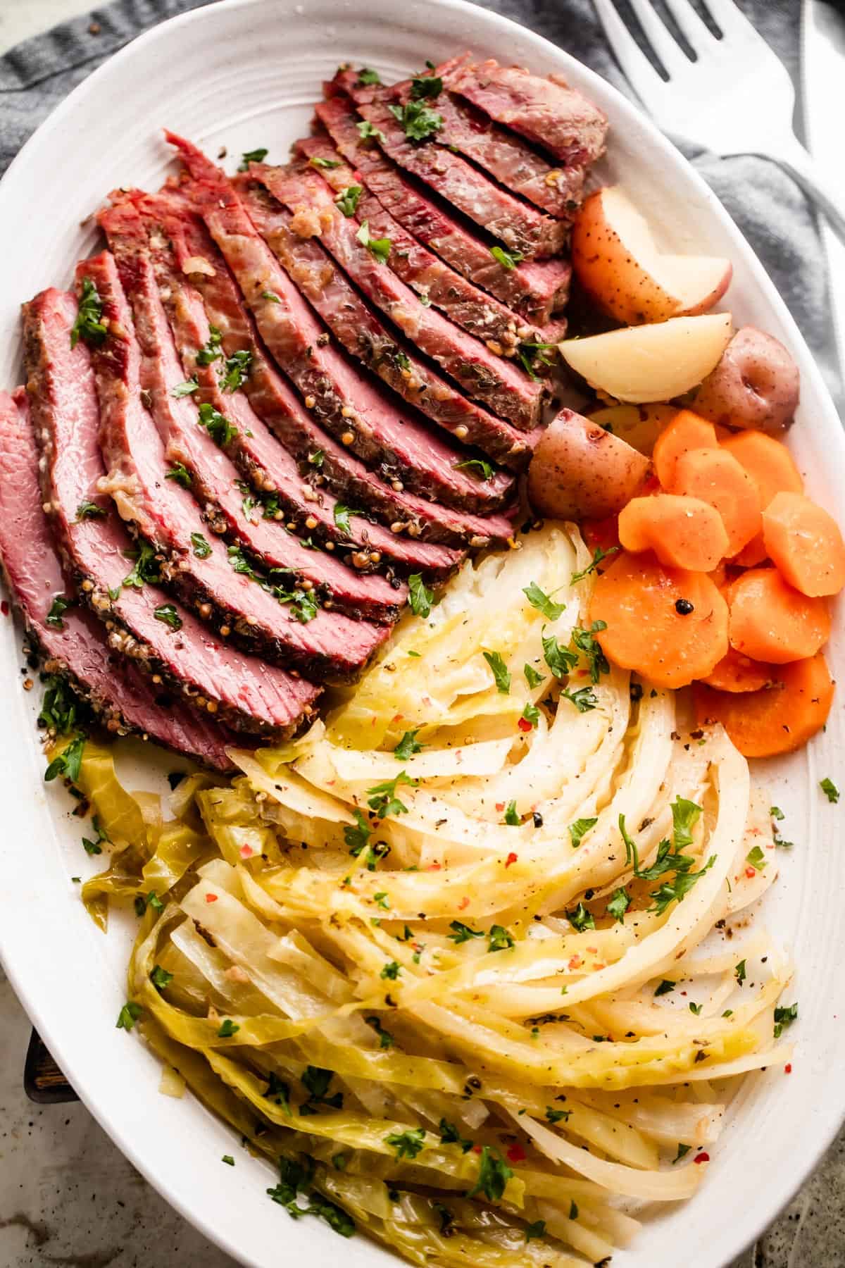 Corned beef on a white serving platter with potatoes, carrots, and cabbage.