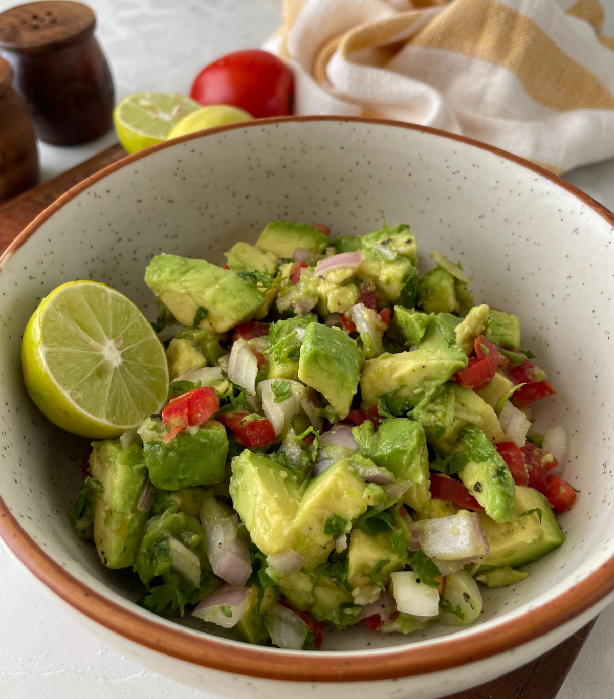 Pico de gallo with avocado and lime in a white bowl.