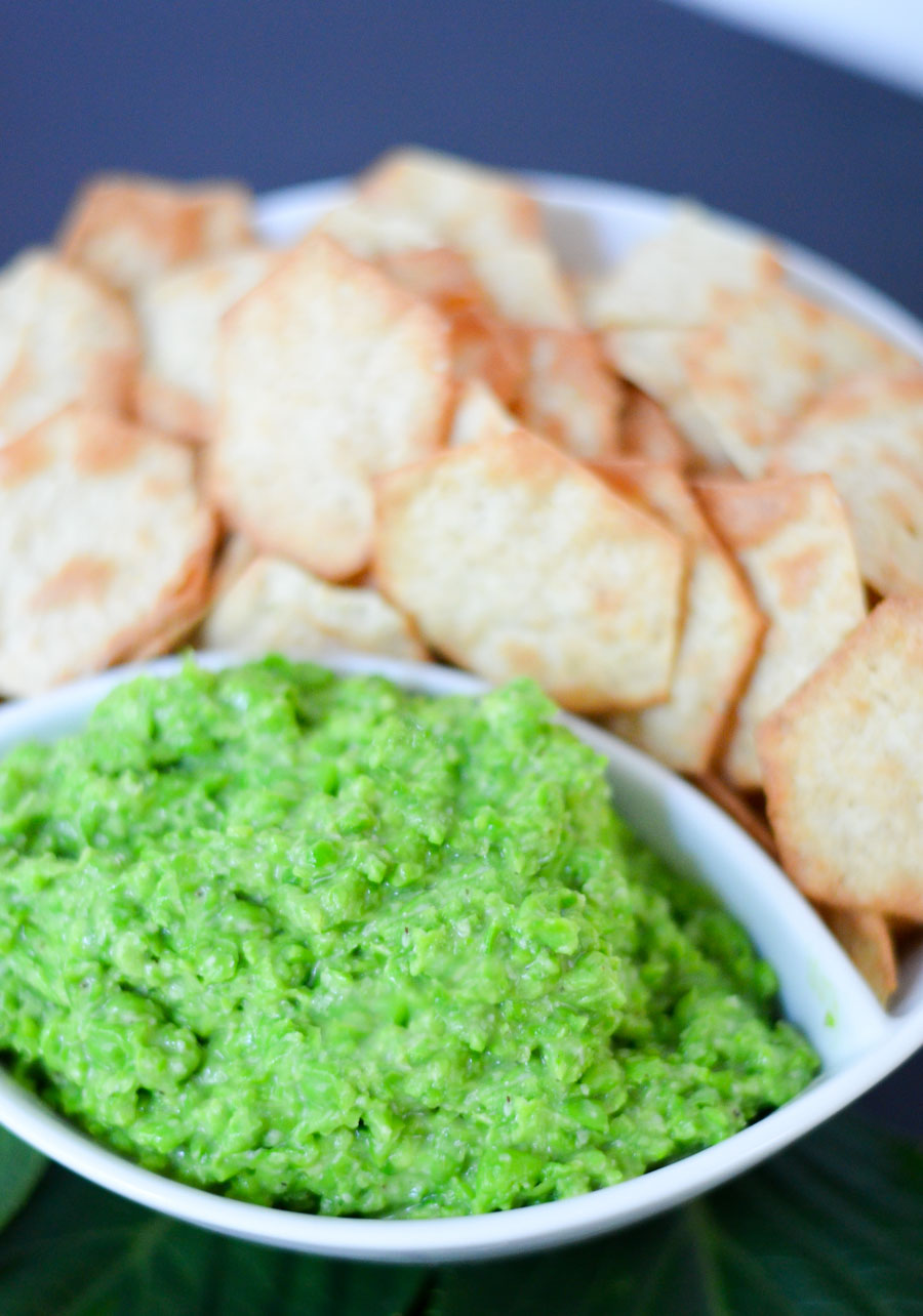 Pea dip in a on a white serving plater with pita chips.