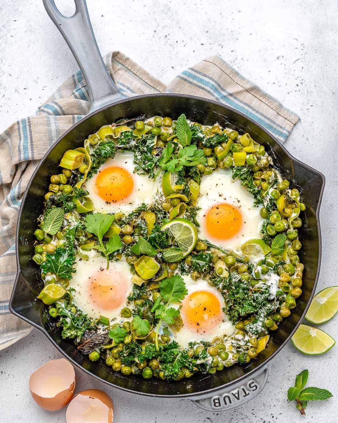 Green shakshuka in a cast iron skillet with lime wedges.