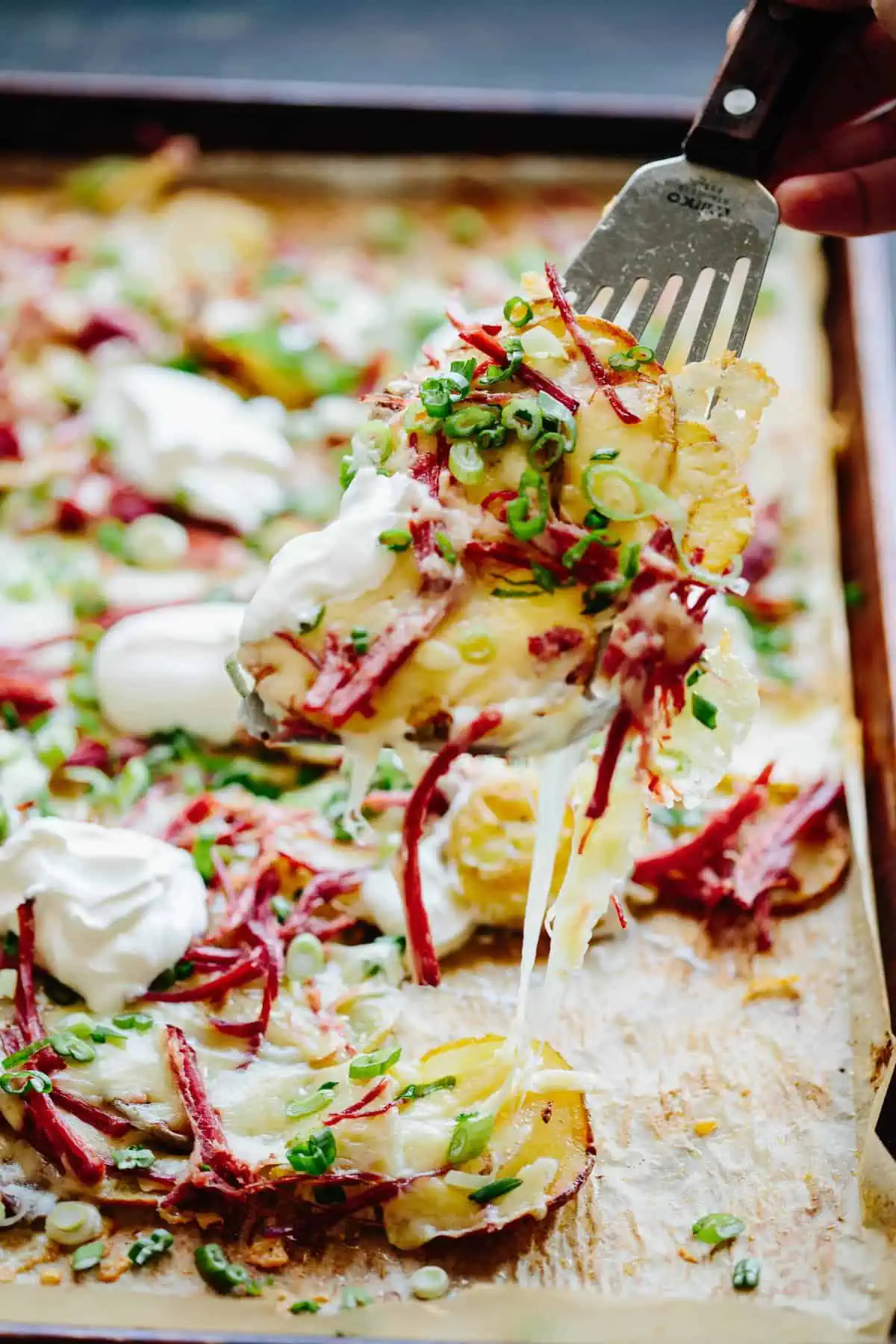A spatula lifts potato slices from a sheet pan filled with Irish nachos.