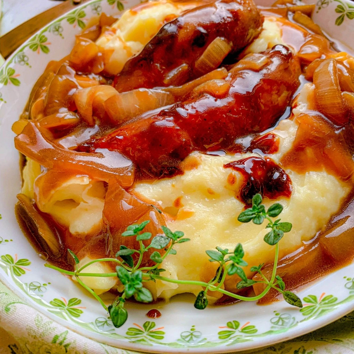 Bangers and mash with gravy and green garnish on a white plate with clovers.