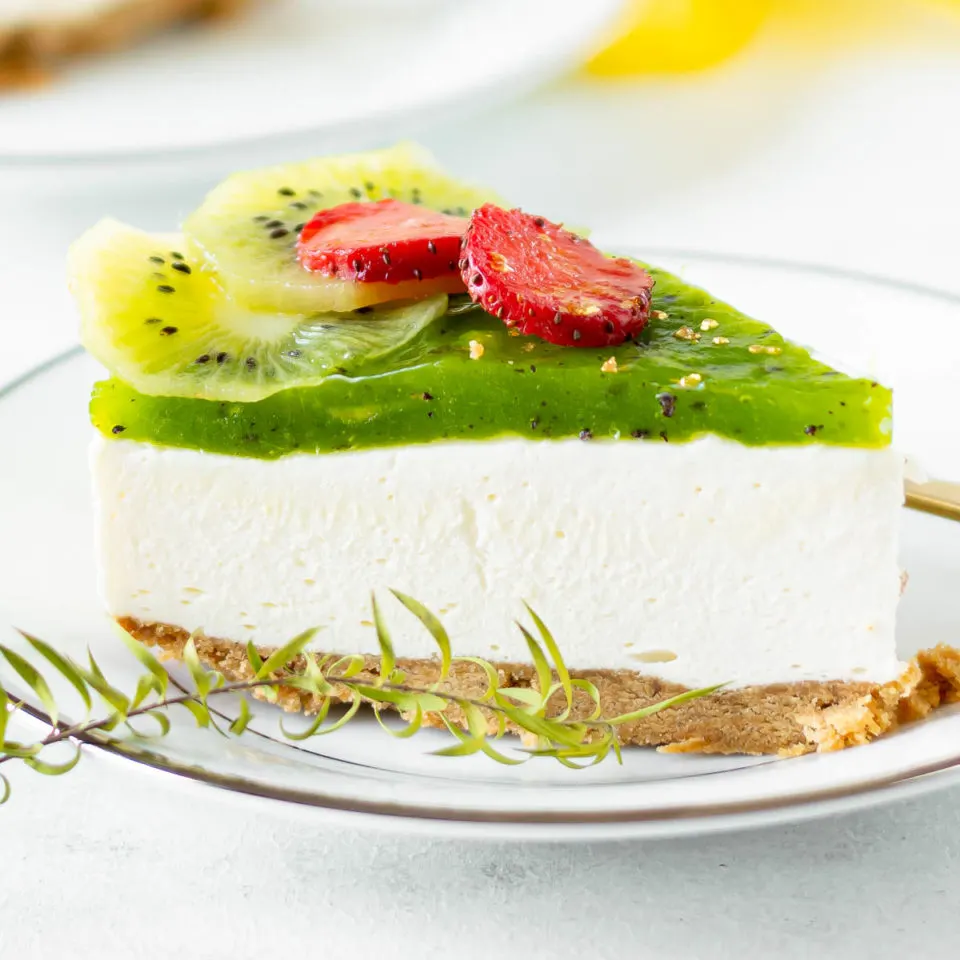 Kiwi cheese cake with kiwi and strawberry garnish on a white plate.