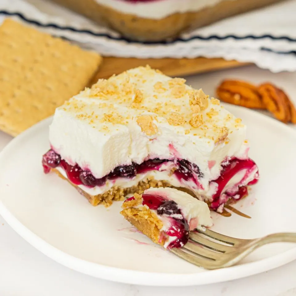 Blueberry delight layered dessert on a white plate with a slice taken out from a fork.