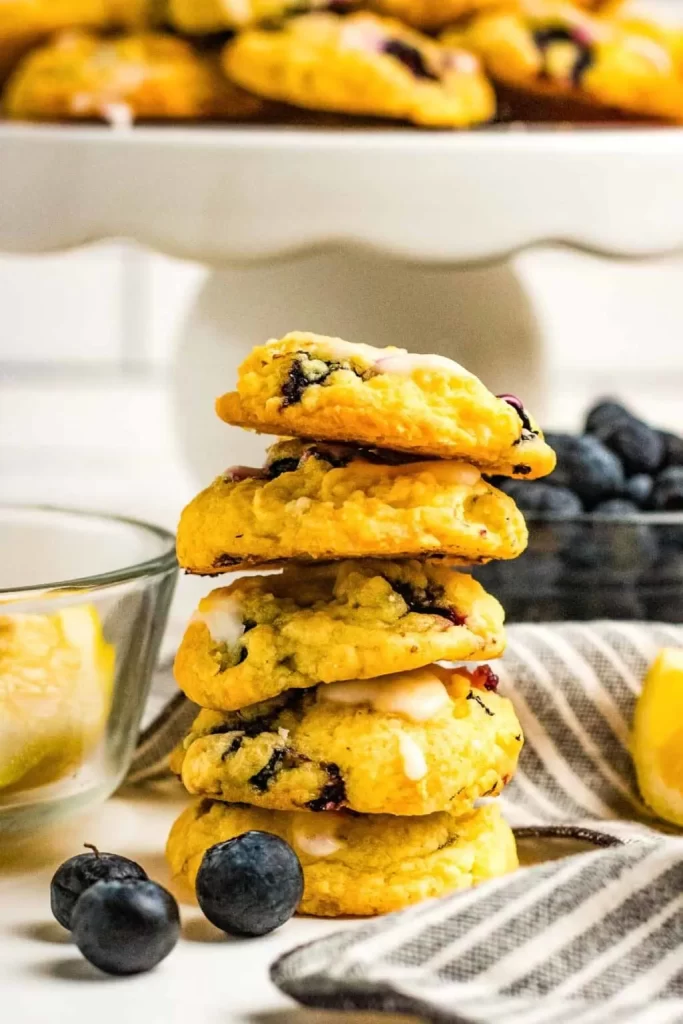 A stack of lemon blueberry cookies in front of food prep bowls with ingredients inside.