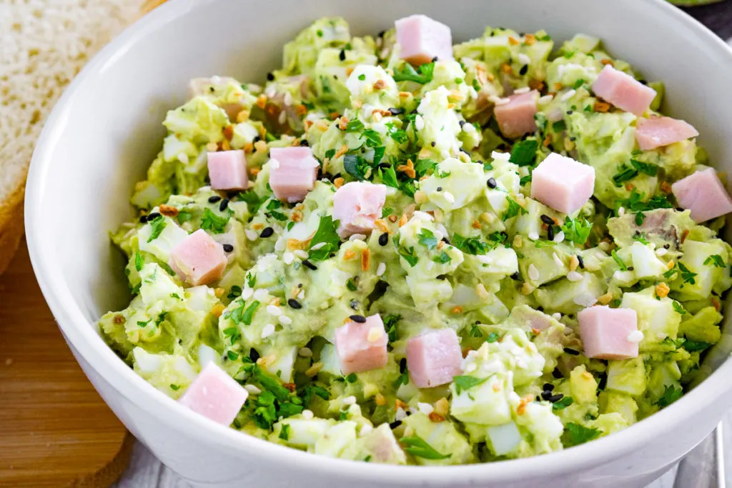 Egg salad with ham and avocado in a large white bowl.