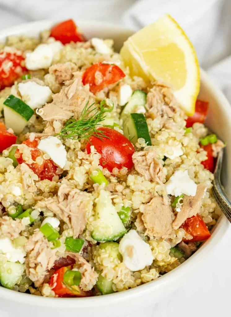 Quinoa tuna salad with tomatoes, cucumber, feta, and a lime wedge.