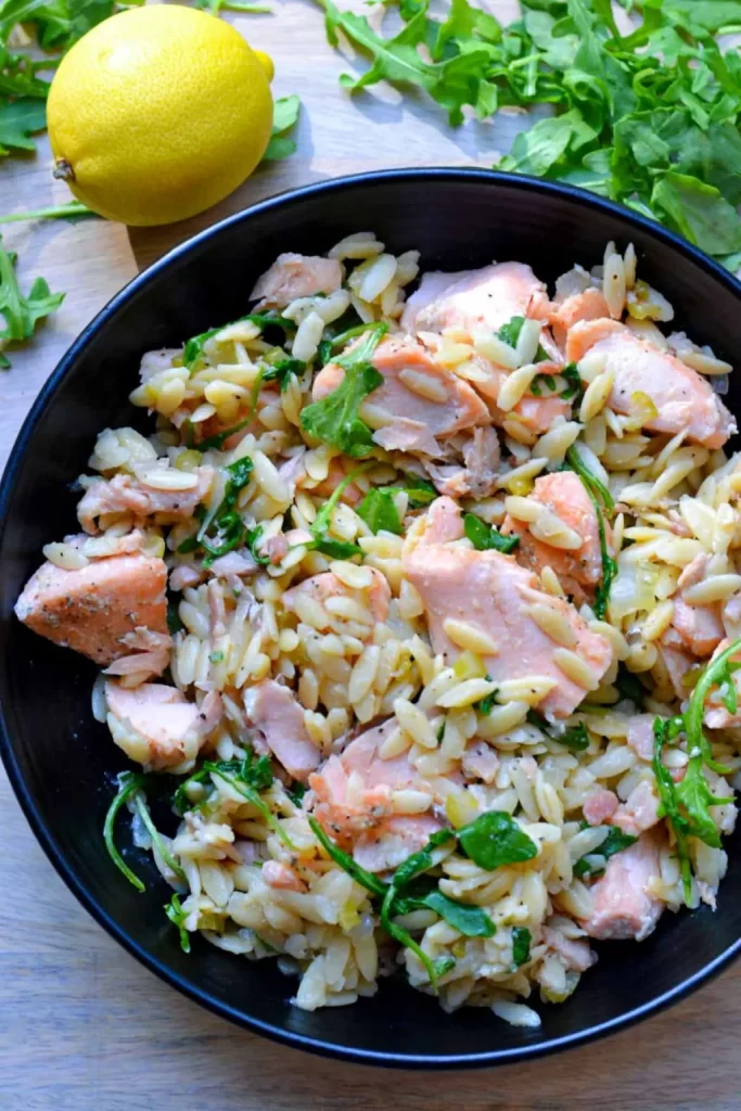 Salmon and orzo with arugula and lemon in a cast iron skillet.