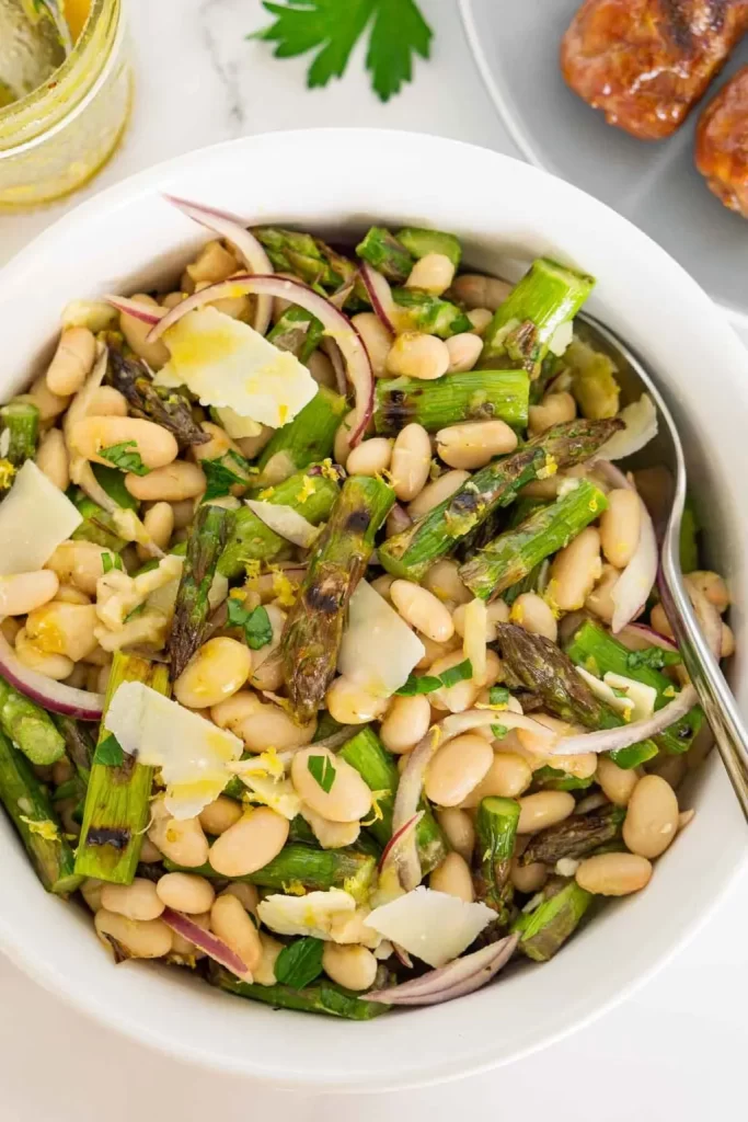 Asparagus and white bean salad with onions in a large white bowl with a spoon.