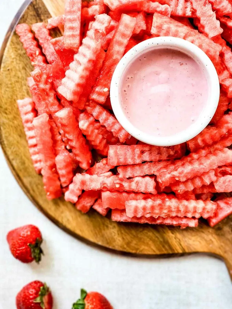 Watermelon fries on a wooden cutting board with strawberry dipping sauce.
