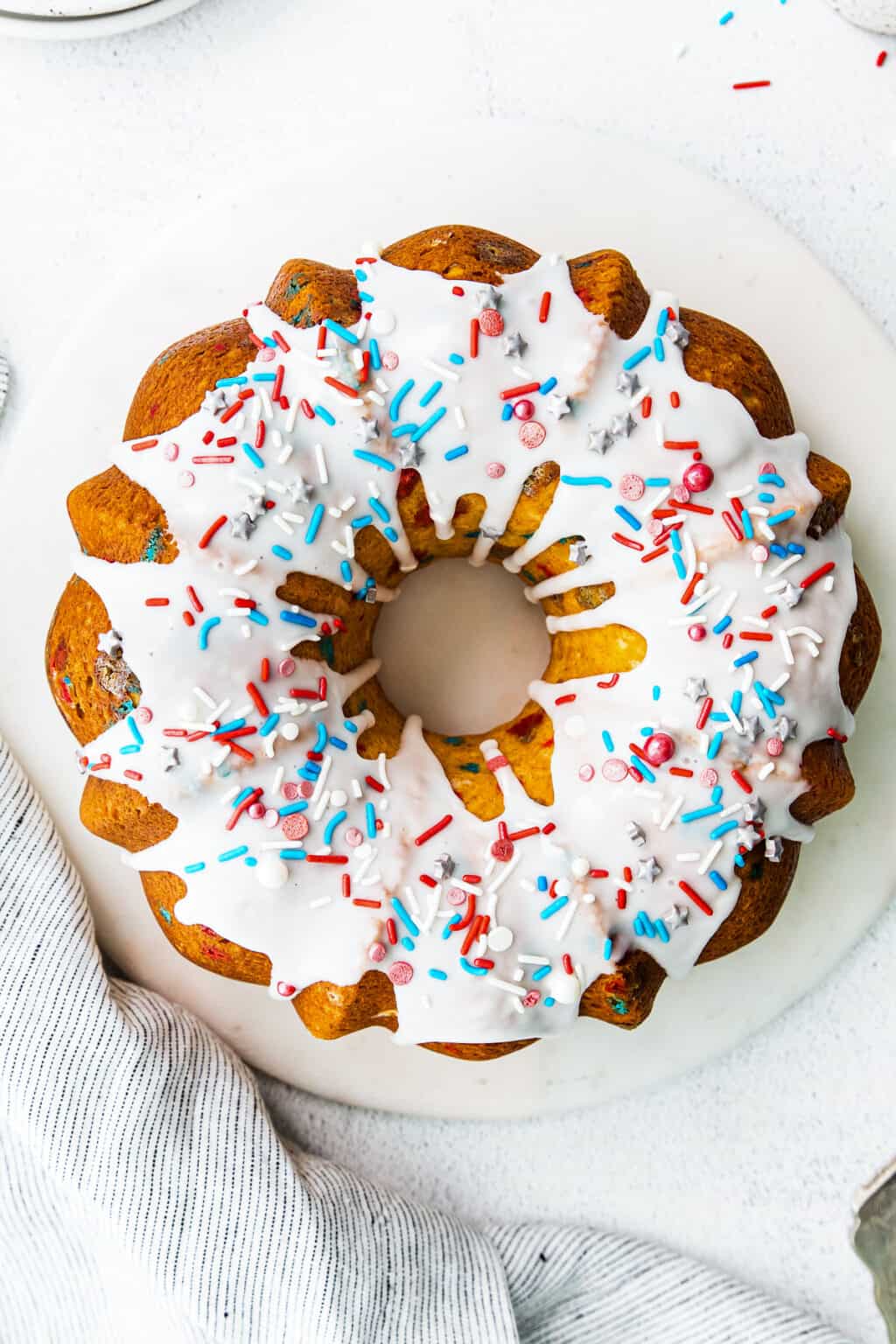 A Bundt cake with white frosting and red, white, and blue sprinkles.