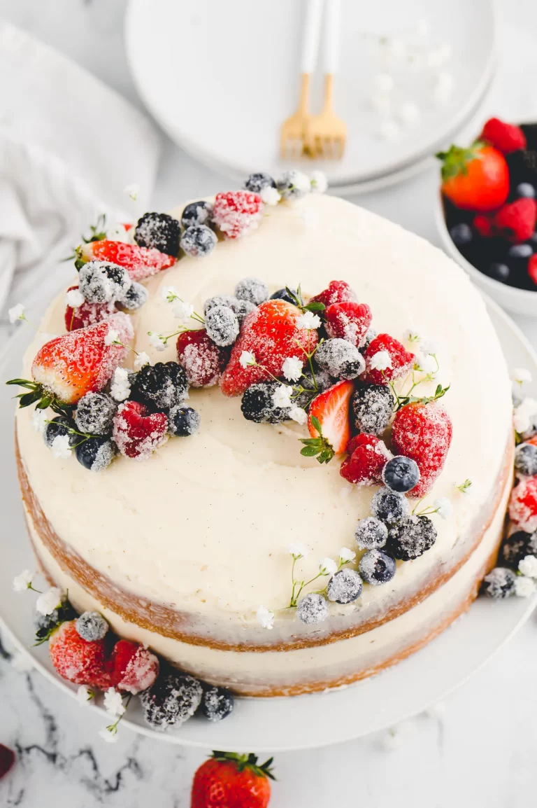 A naked vanilla cake with strawberries and blueberries on top.