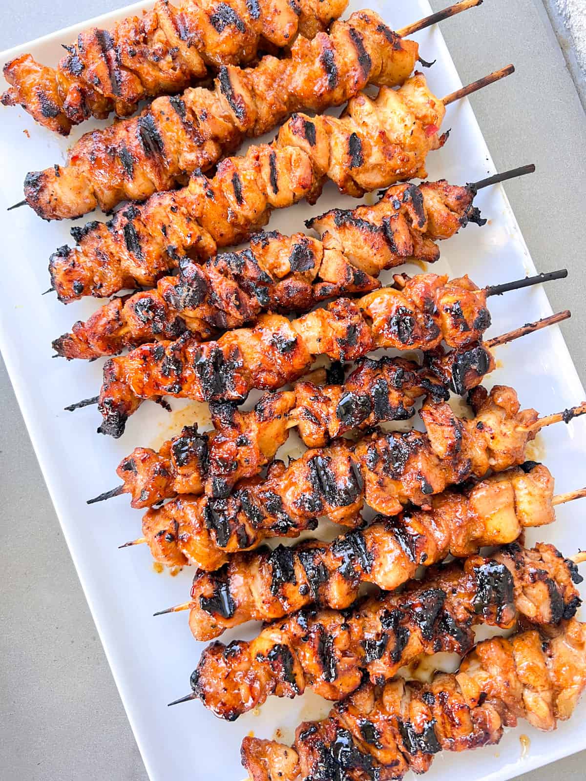 Grilled sweet chili sauce chicken skewers on a large white rectangular serving platter.