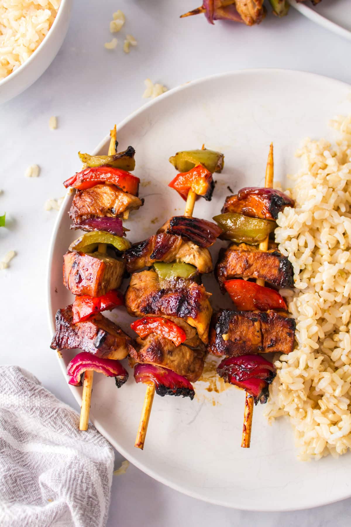 Grilled chicken kabobs with vegetables next to rice on a white plate.
