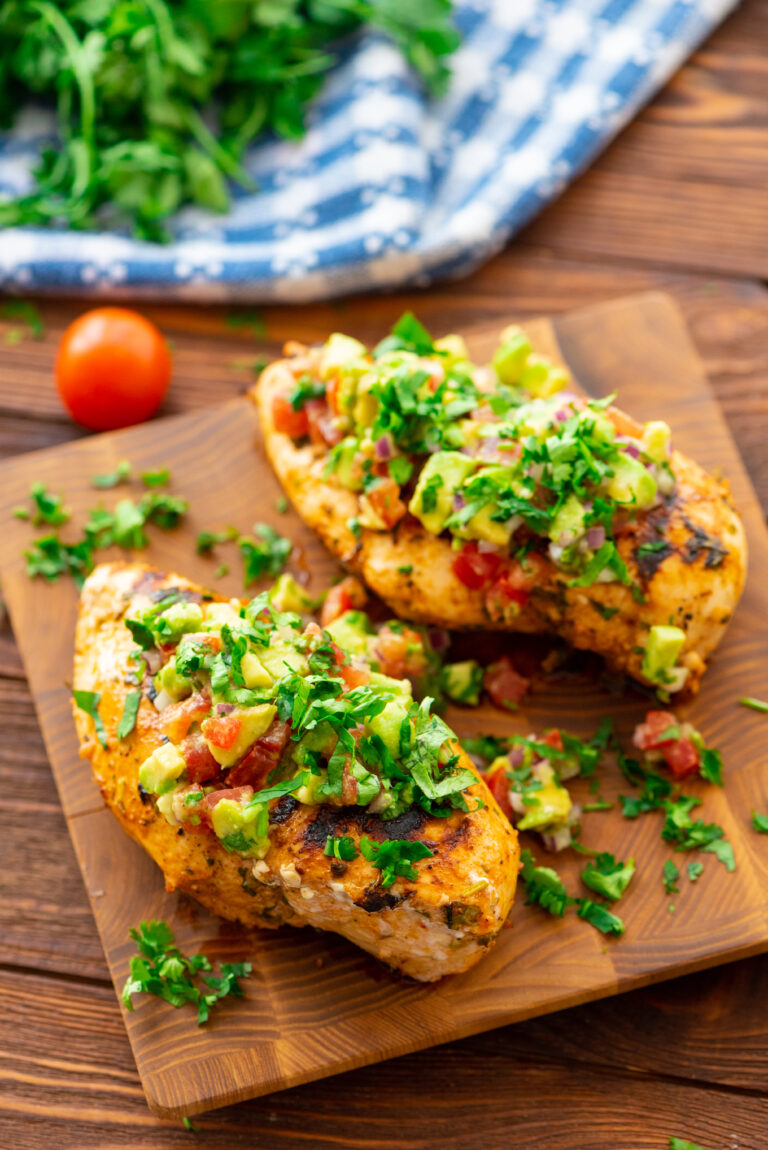 Grilled chicken with breasts on a wooden cutting board with toppings.