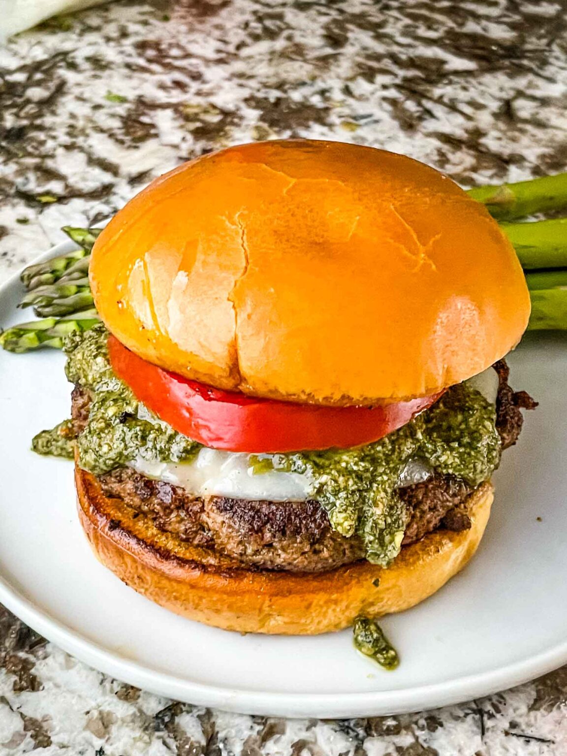 A Turkey burger with pesto sauce and a tomato sliced on a white plate.