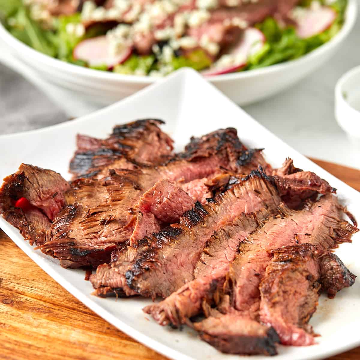 Grilled flank steak on a rectangular white serving platter.