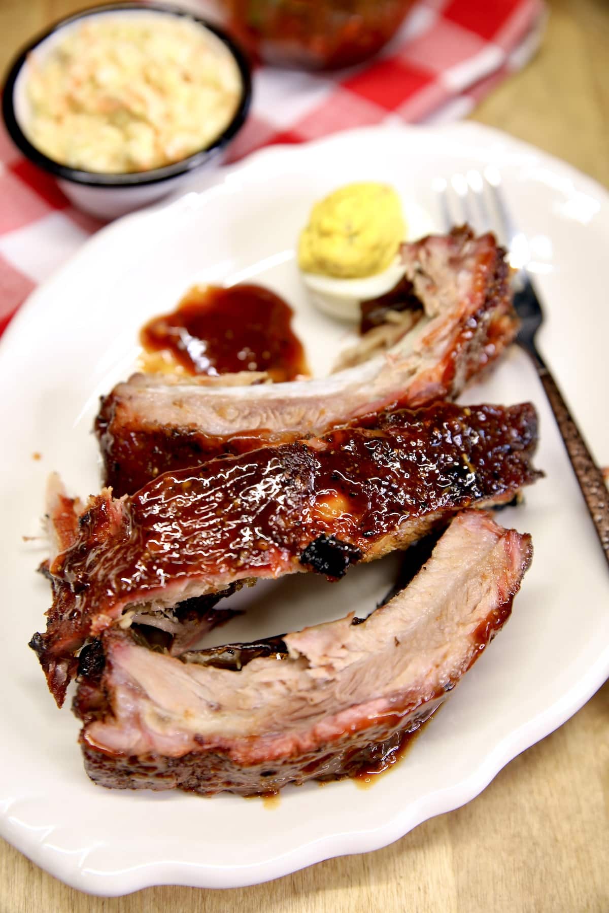 BBQ baby back ribs on a white plate with a deviled egg.
