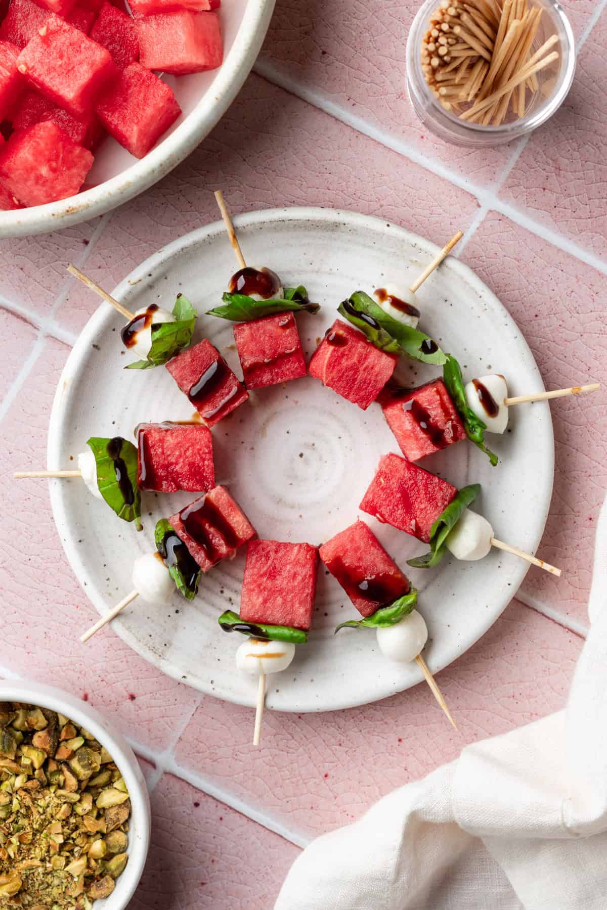 Caprese watermelon skewers with basil and balsamic glaze on a white plate.