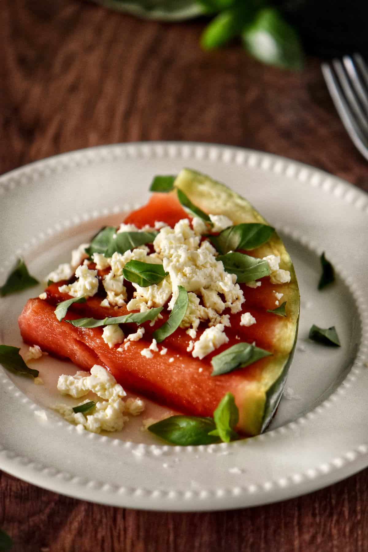 Watermelon steak with feta, balsamic glaze, and green garnish.