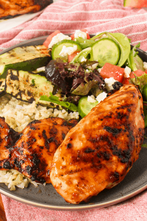 Grilled watermelon chicken on a plate with rice and a side salad.