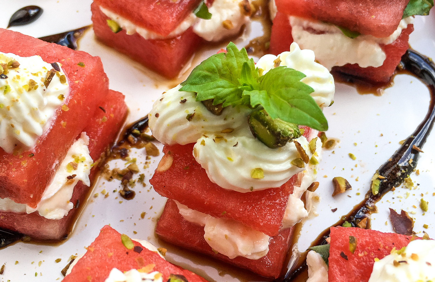 Watermelon whipped feta bites with balsamic glaze and green garnish.