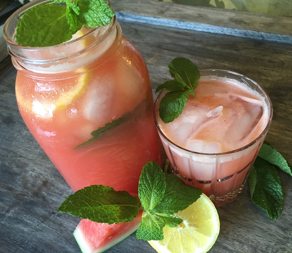 Watermelon lemonade in a mason glass jar ad a class cup with green garnish.