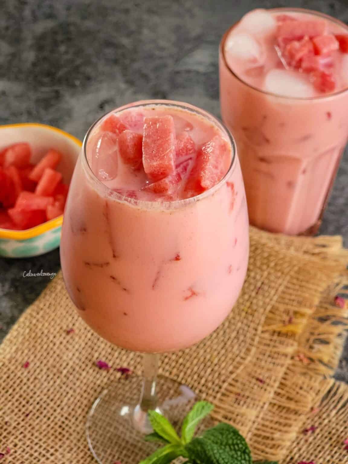 Watermelon rose drink in two glasses next to a bowl of diced watermelon.