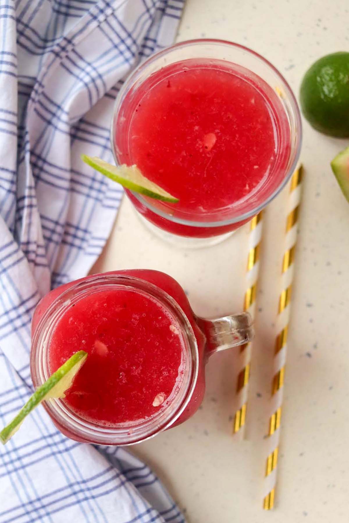 Watermelon lime slushies in two glasses with lime garnish and gold and white striped stars.