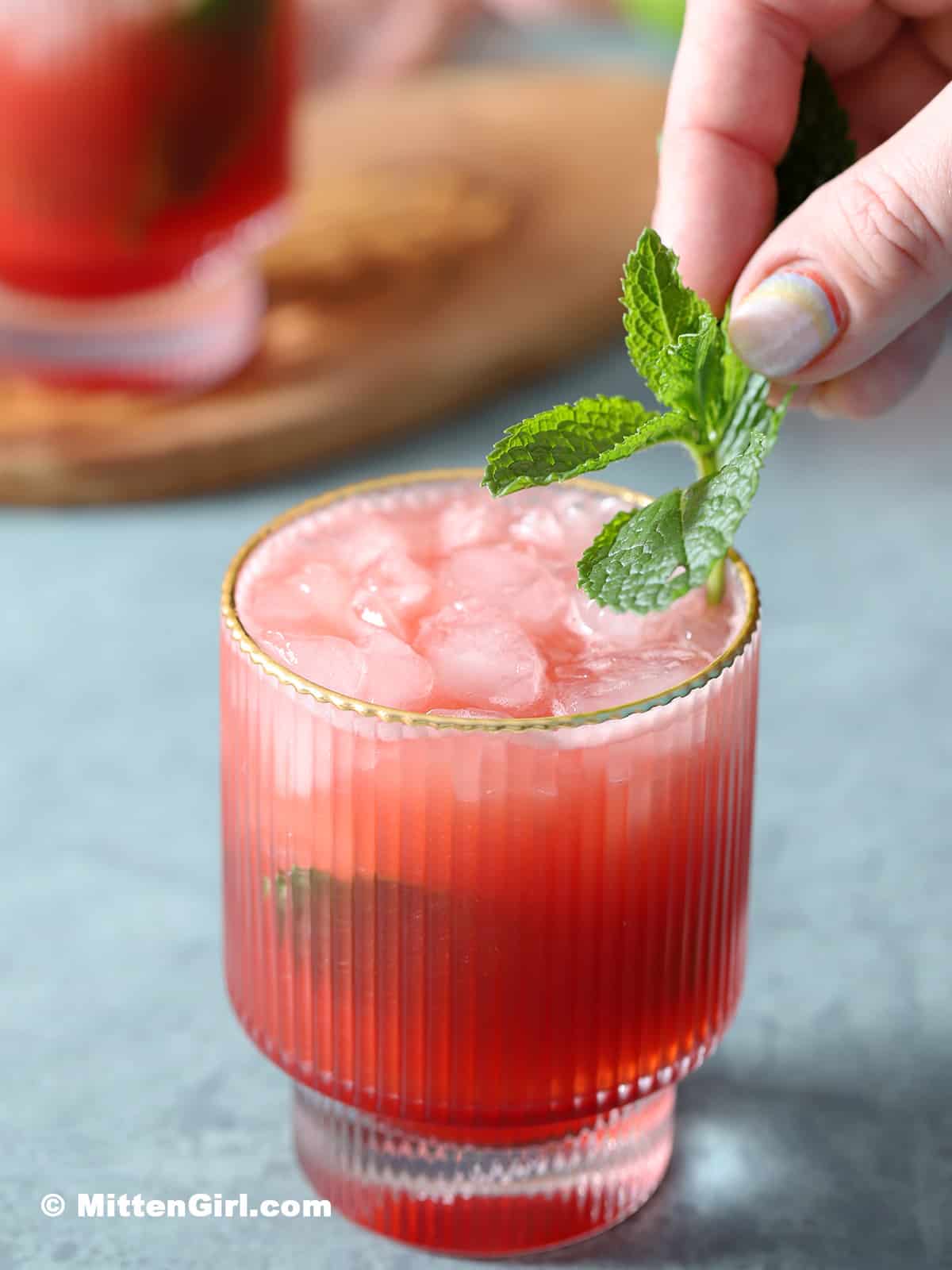 A watermelon strawberry mocktail in a short glass with green garnish.