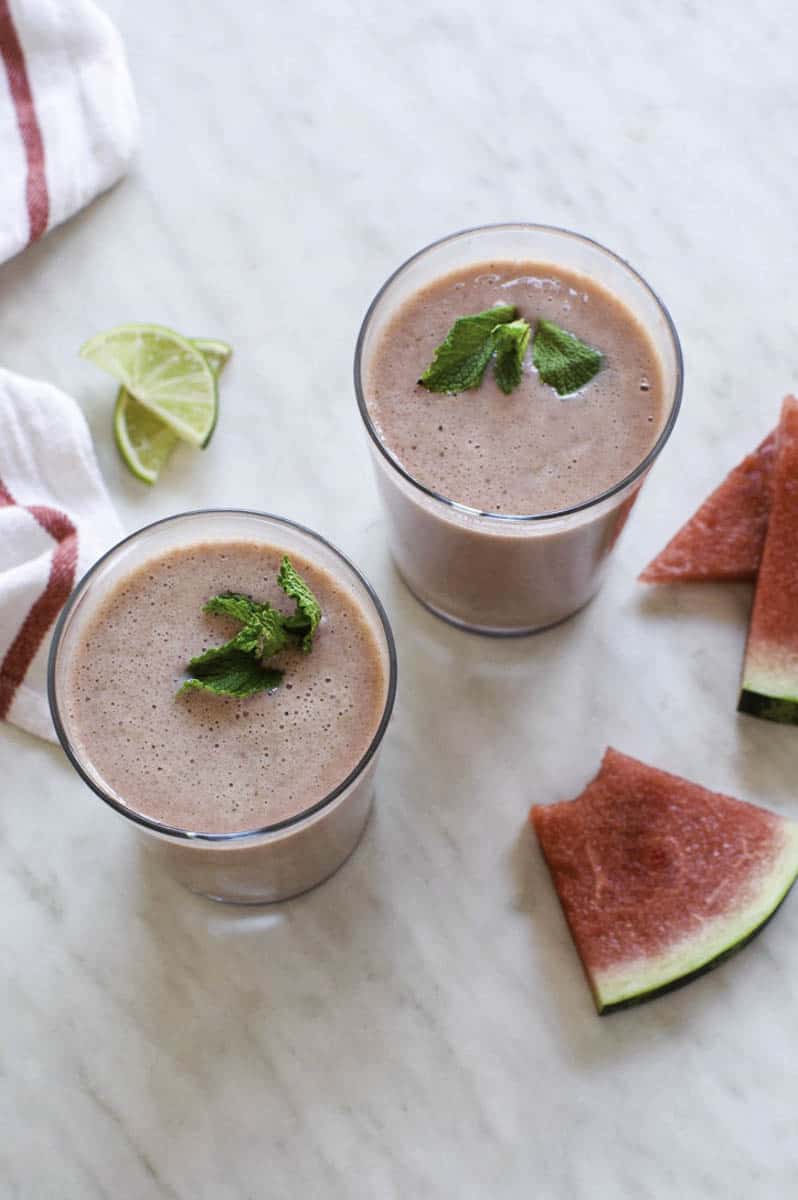 Watermelon mango smoothies in two glasses with green garnish.