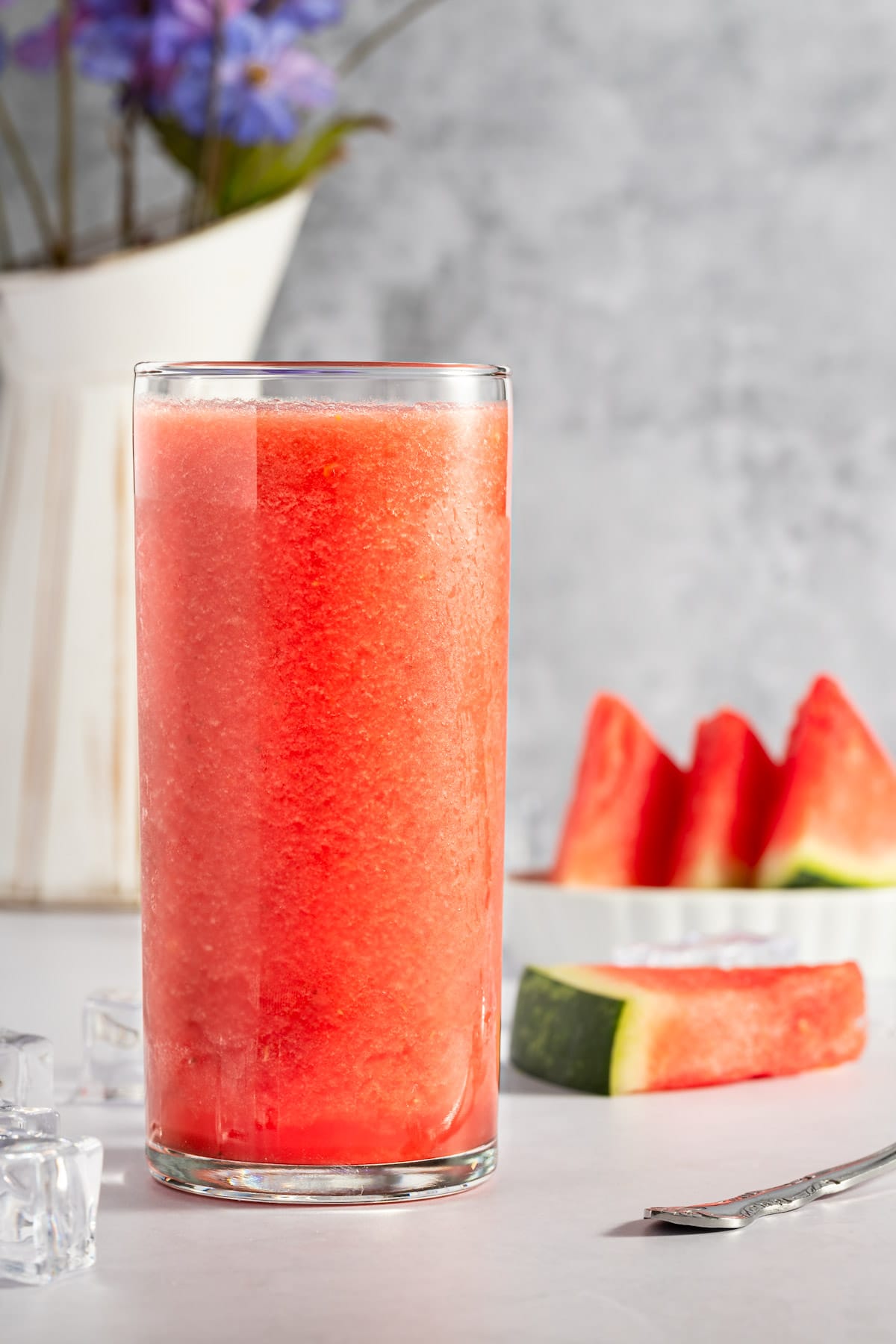 A watermelon banana smoothie and a tall clear glass with watermelon wedges behind it.