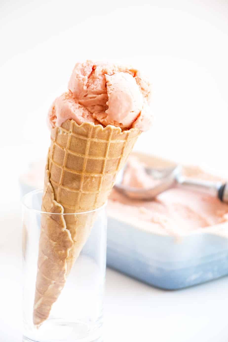 Watermelon coconut ice cream in a cone and a dish with an ice cream scoop.