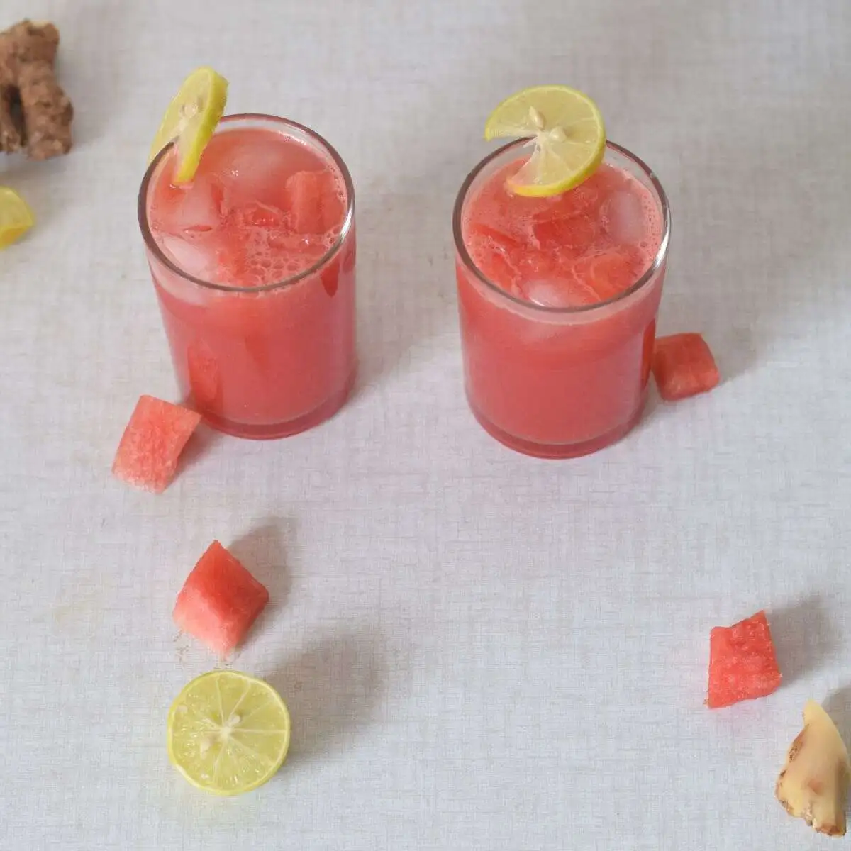 Watermelon ginger juice in two glasses with lime wedge garnish.