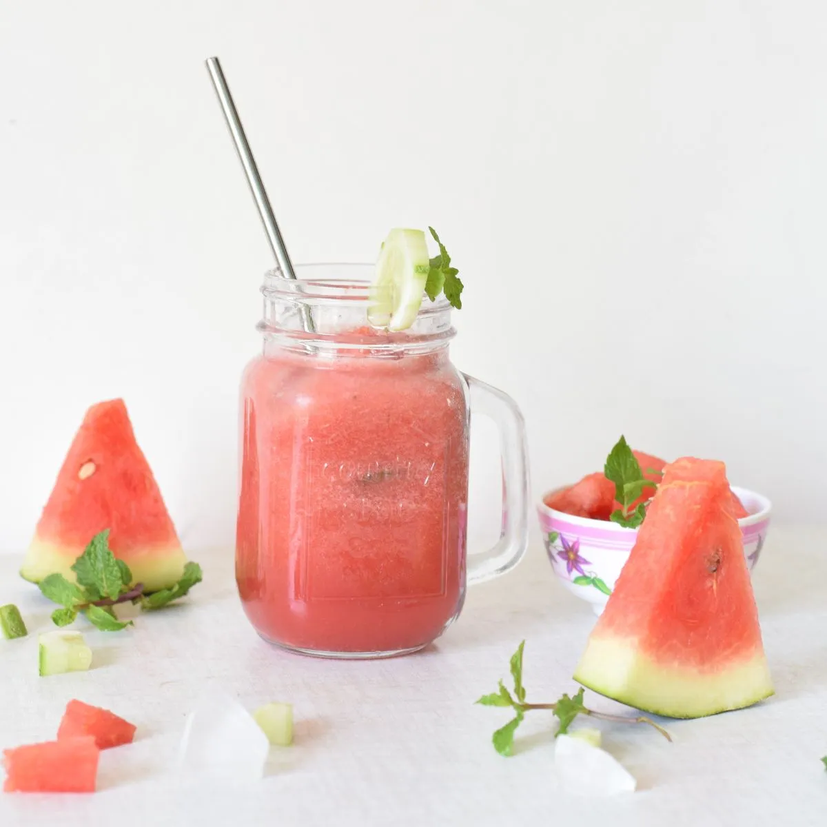 A watermelon cucumber drink in a mason glass jar with cucumber garnish and a straw.
