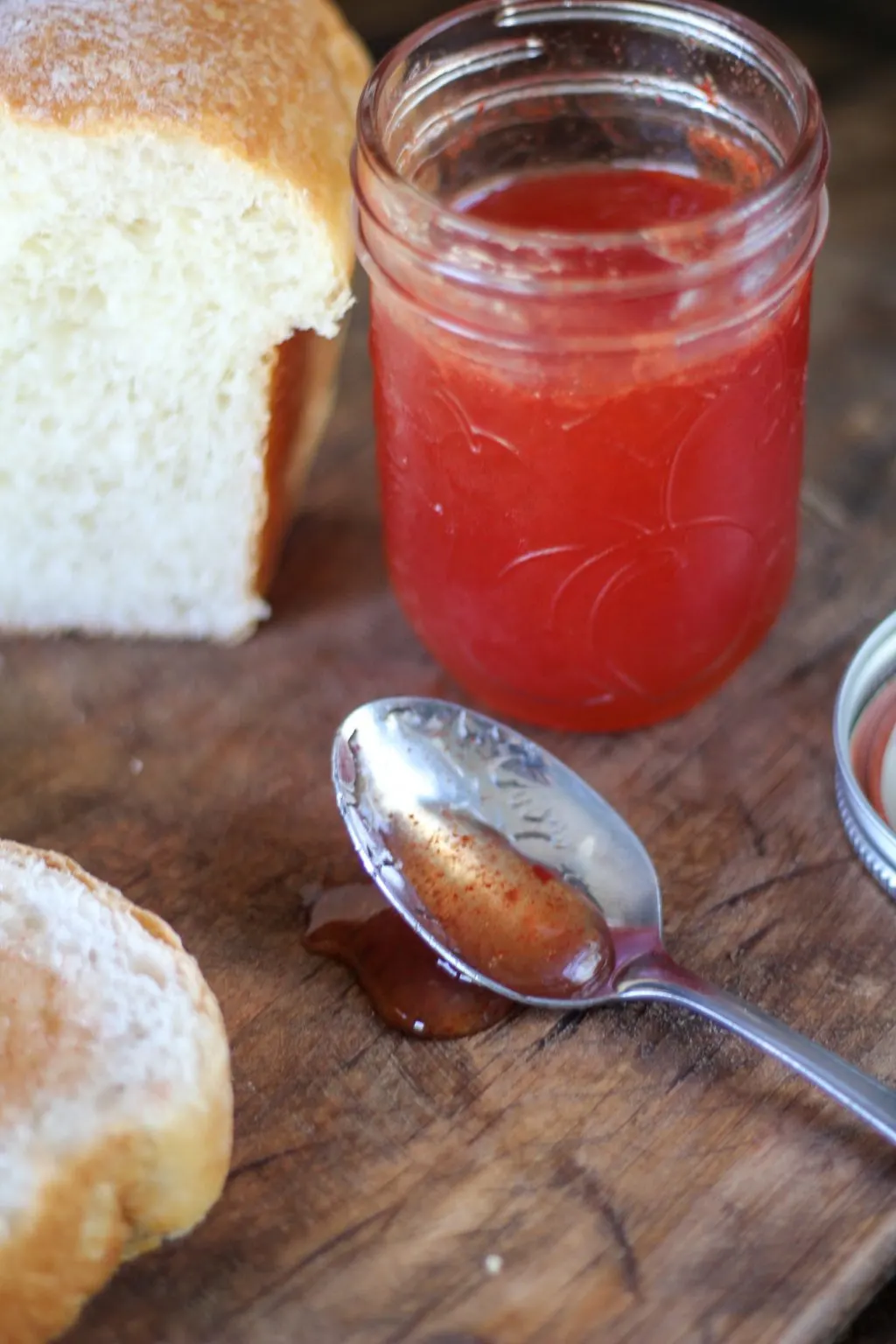 Watermelon jelly in a mason jar next to a sliced loaf of bread with jelly on it.
