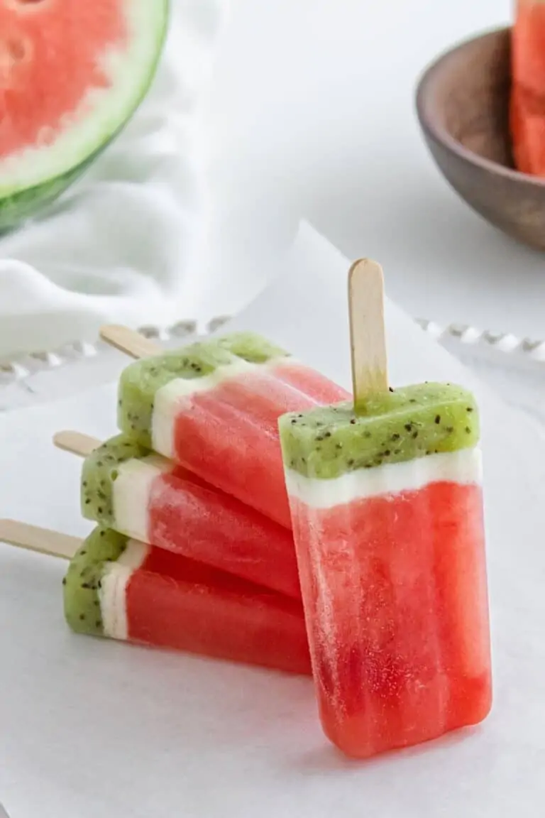 Red, white, and green watermelon popsicles with a sliced watermelon in the background.