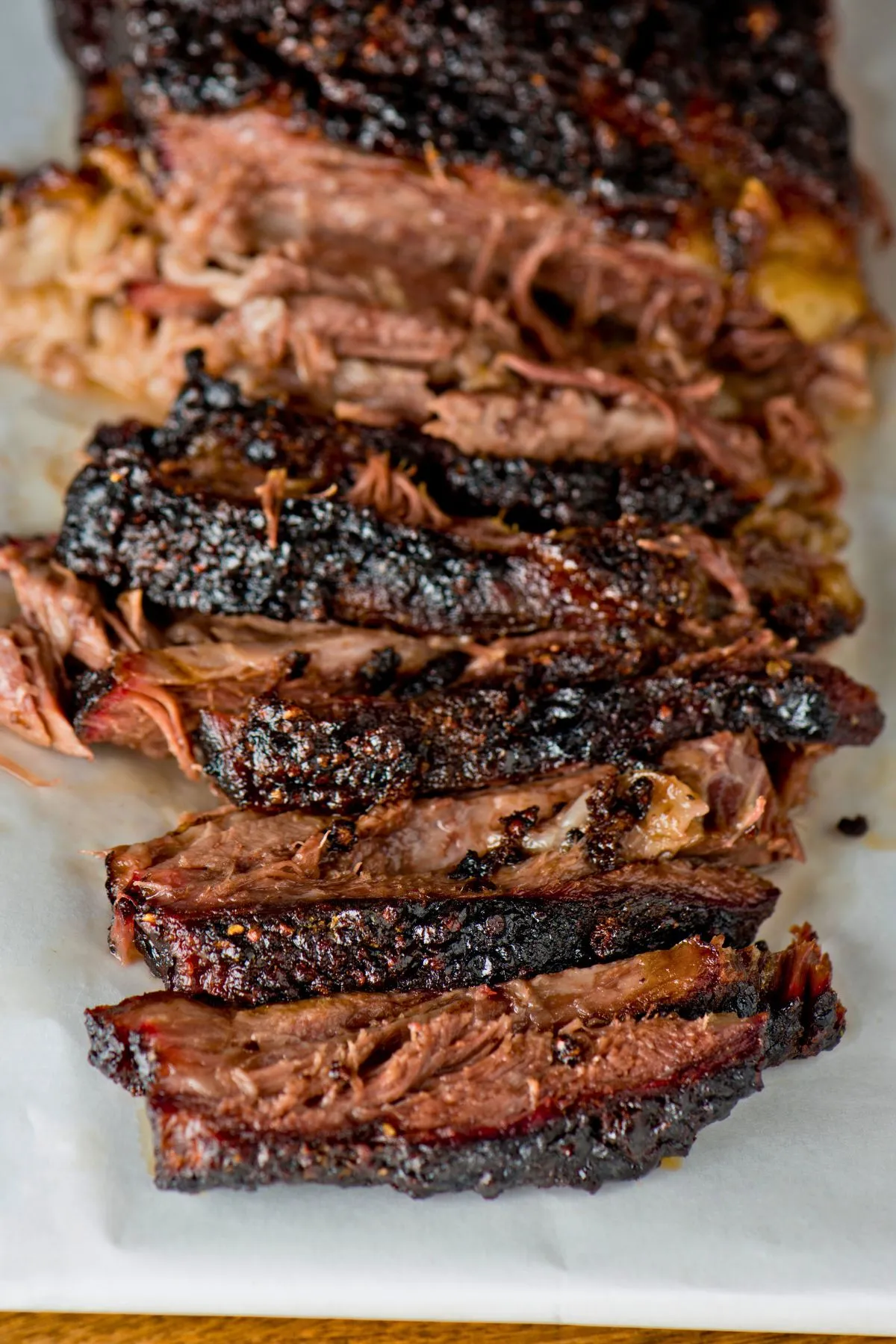 Sliced beef brisket with dark crispy bark on parchment paper.