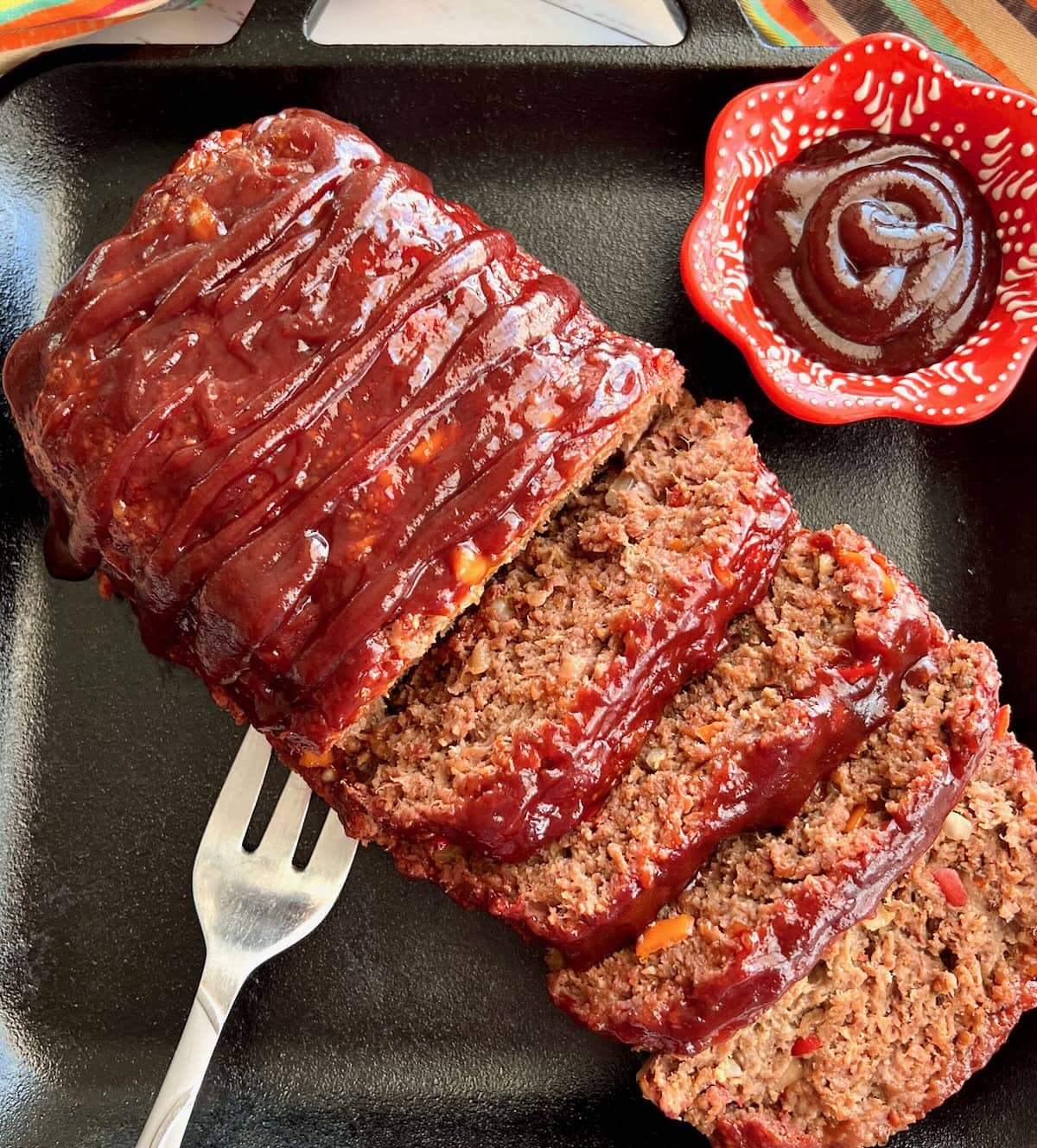 A sliced log of smoked meatloaf with a side of BBQ sauce.