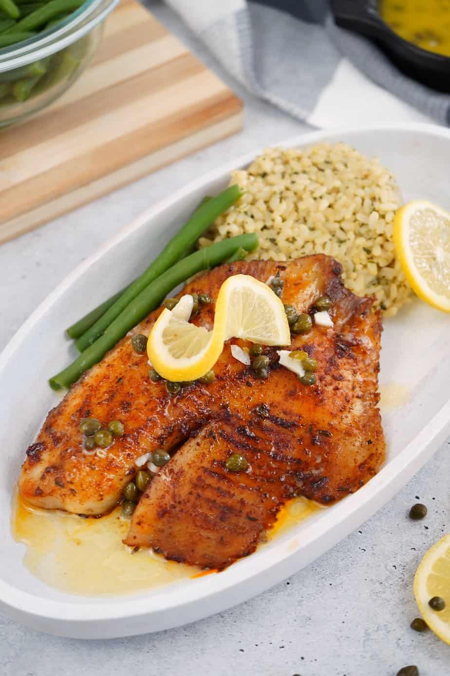 Smoked tilapia with rice, green beans, and lemon on a white plate.