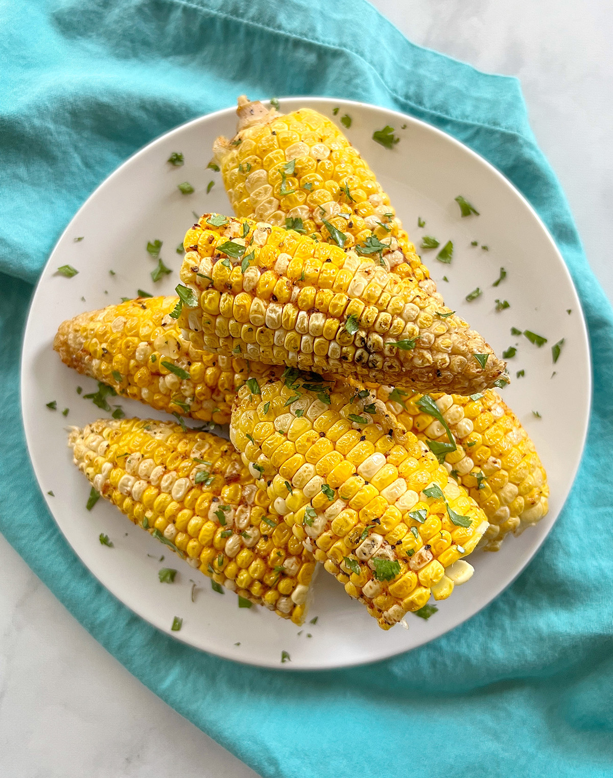 Several ears of smoked corn on the cob piled on a white plate.