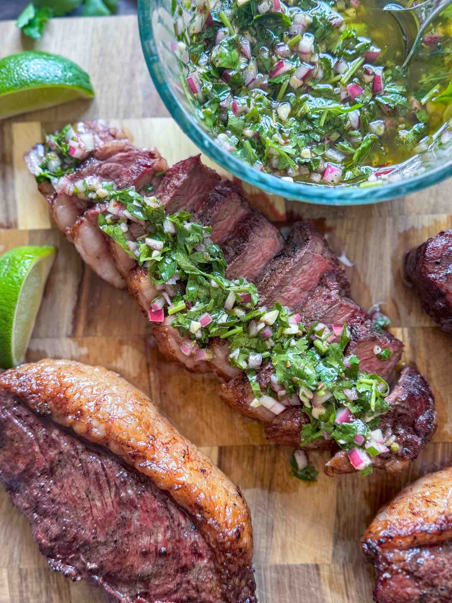 Smoked steak with green sauce on a wooden cutting board.
