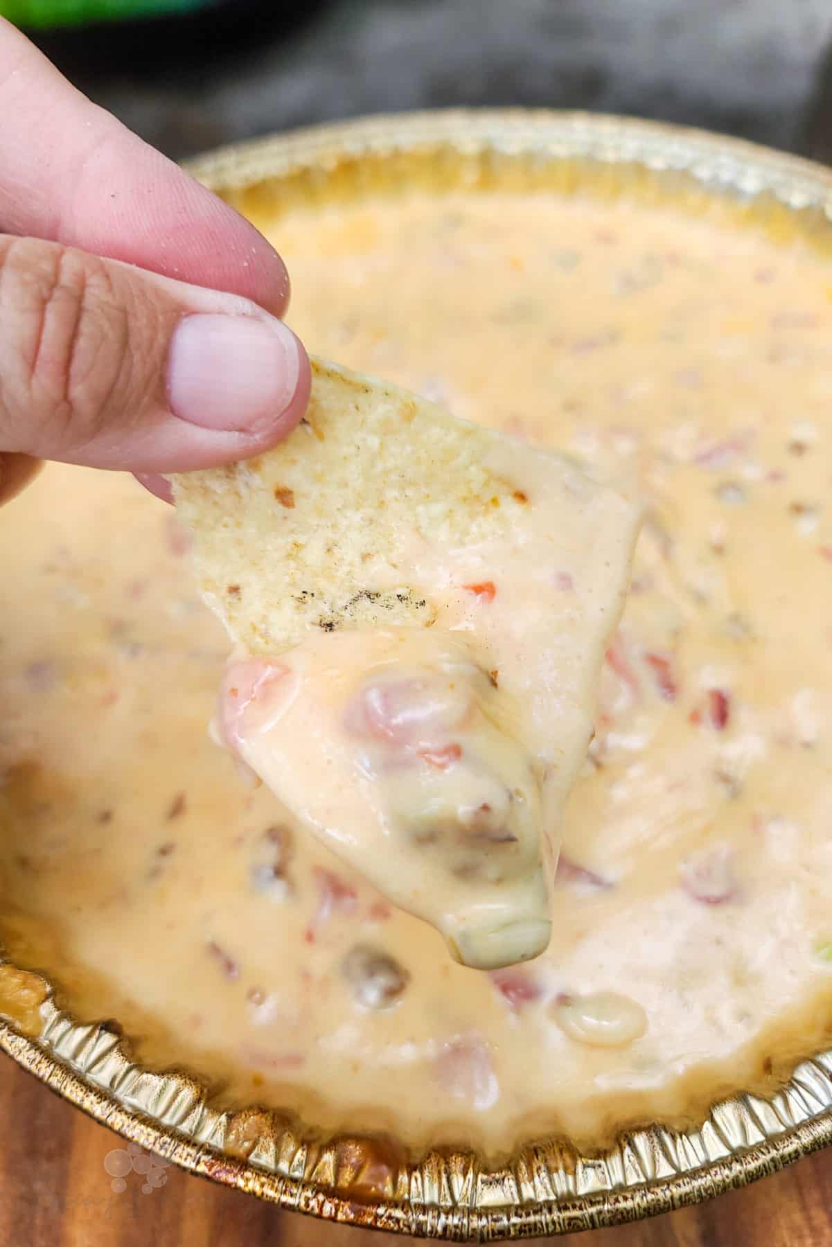 A woman dips a tortilla chip into a dish of smoked queso.