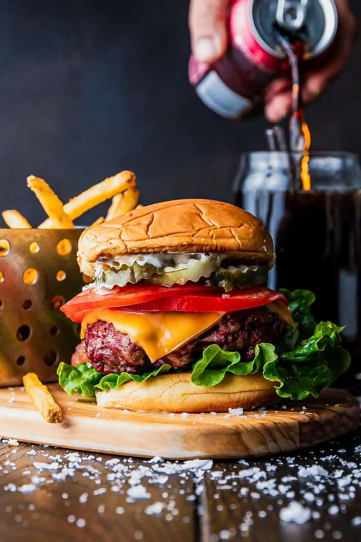 A large burger with cheese, tomatoes, and pickles next to a basket of fries.