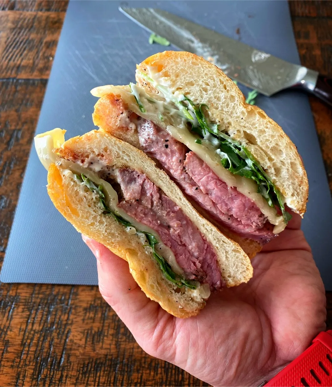 A person holds to halves of a cut steak sandwich over a cutting board.