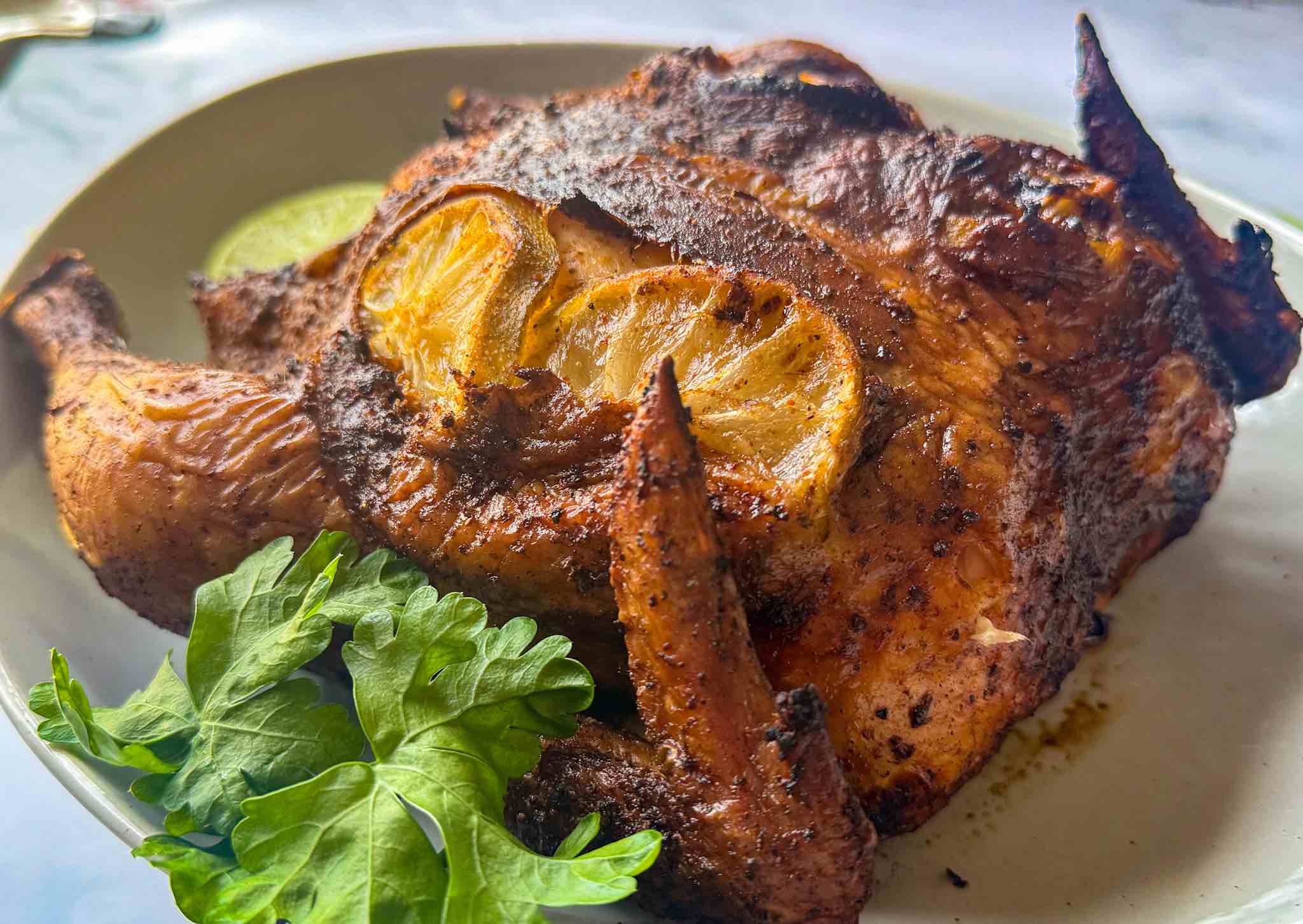A whole smoked chicken on a serving platter with lettuce leaves and lemon slices.