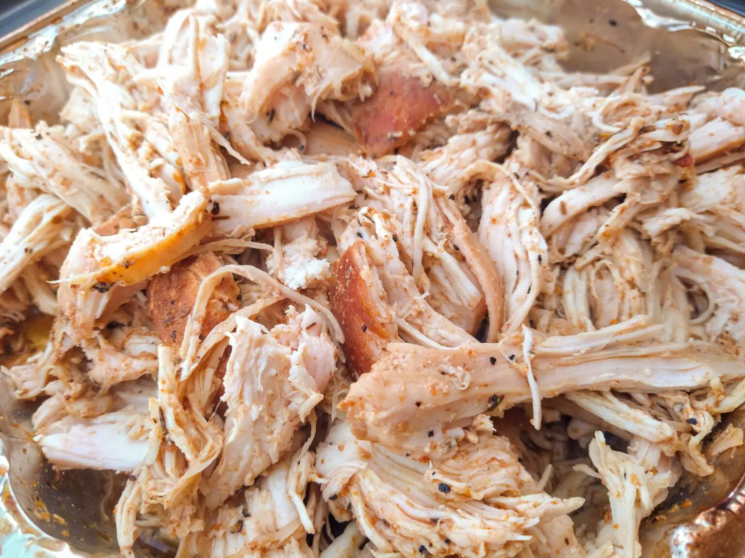 A close-up of smoked and shredded pulled chicken in a tin pan.
