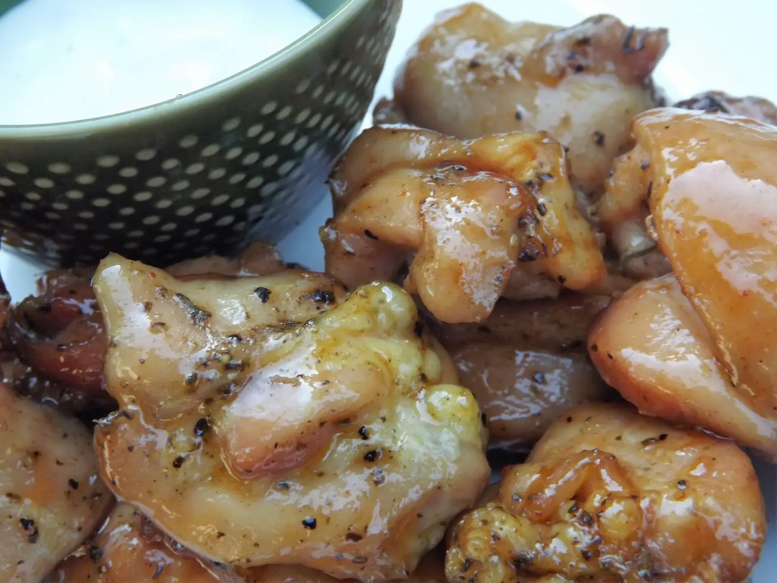 Smoked chicken bites on a serving platter next to a bowl of white dipping sauce.