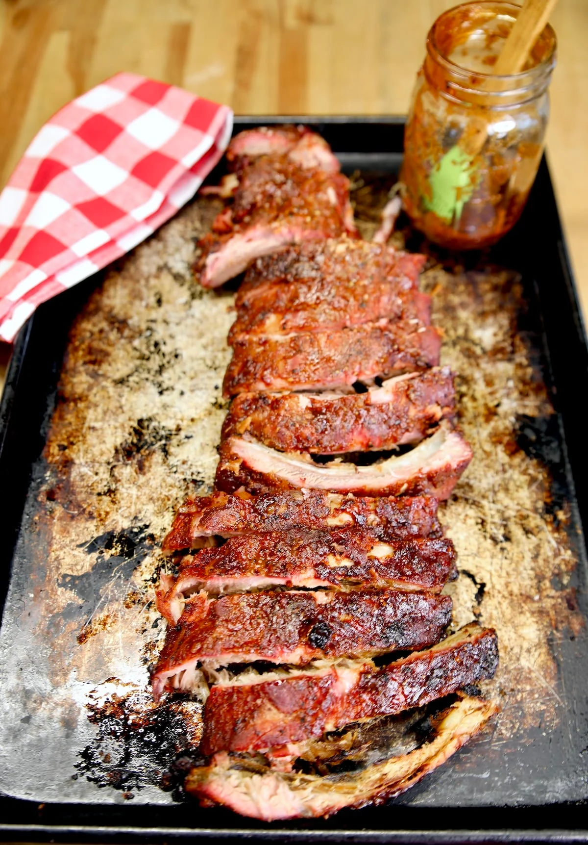 Smoked pork ribs on a sheet pan with a red and white checkered cloth.