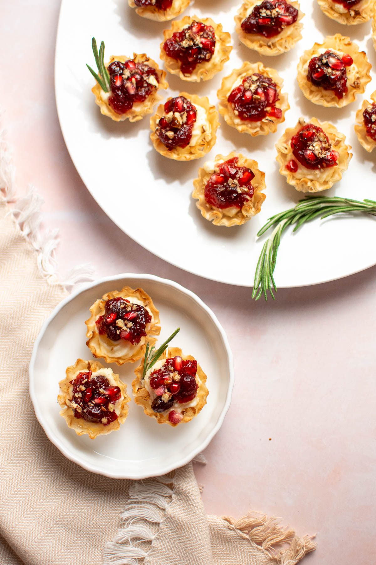 Dish of cranberry brie bites on small dish next to white platter full of bites.